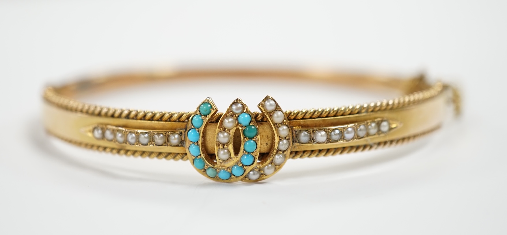 A 9ct gold, seed pearl and turquoise set twin horseshoe motif hinged bangle, gross weight 7.5 grams.